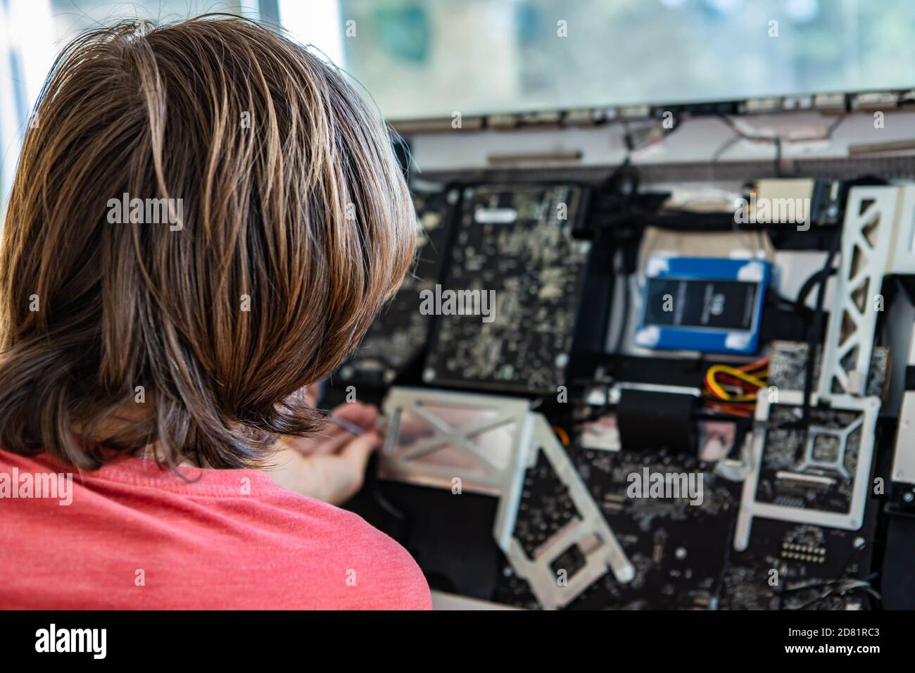 Vista posteriore di un giovane tecnico maschile con fissaggio lungo dei capelli e risolvere il problema con il computer desktop rotto in ufficio utilizzo degli strumenti Foto Stock