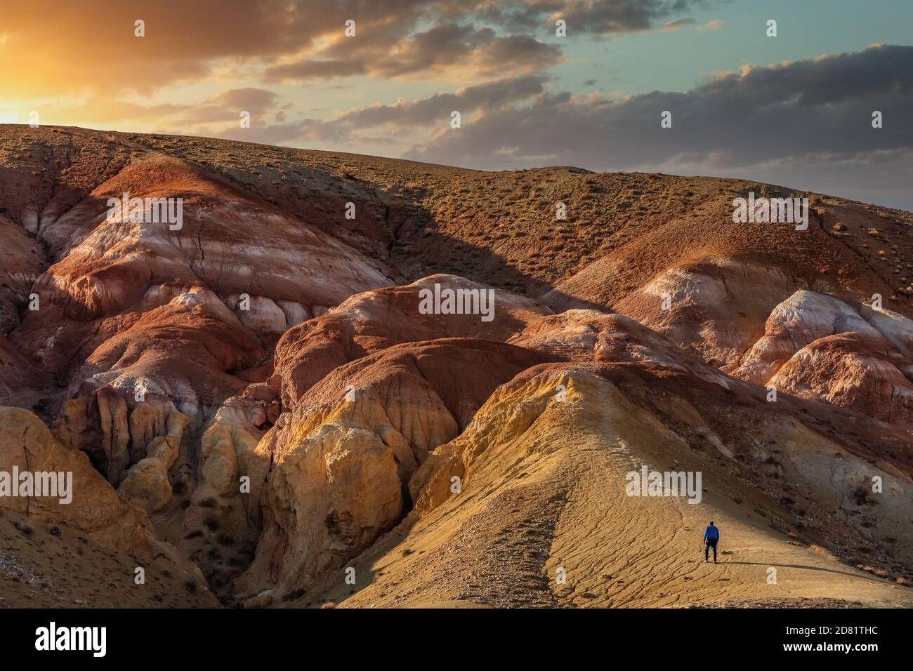 Foto ad alto angolo di un turista che arrampica massicce montagne rosse nella valle di Kyzyl-Chin, chiamata anche valle di Mars. Bellissimo cielo nuvoloso tramonto come sfondo Foto Stock