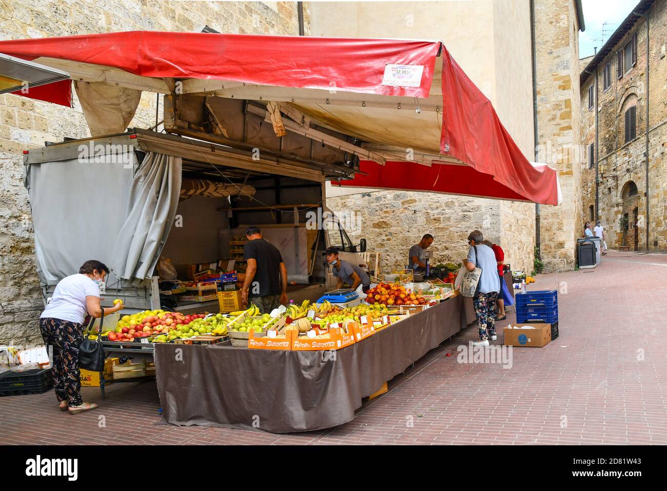 La gente acquista in un mercato di frutta e verdura nel centro storico di San Gimignano, patrimonio dell'umanità dell'UNESCO, Siena, Toscana, Italia Foto Stock