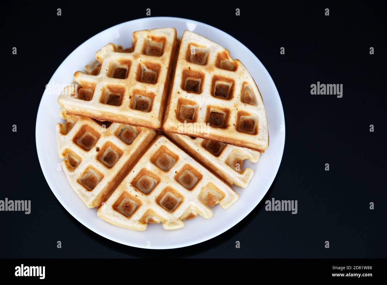 Waffle belgi in piatto bianco su tavolo di vetro nero. Colazione sana, pezzi di wafer classico appena sfornato Foto Stock
