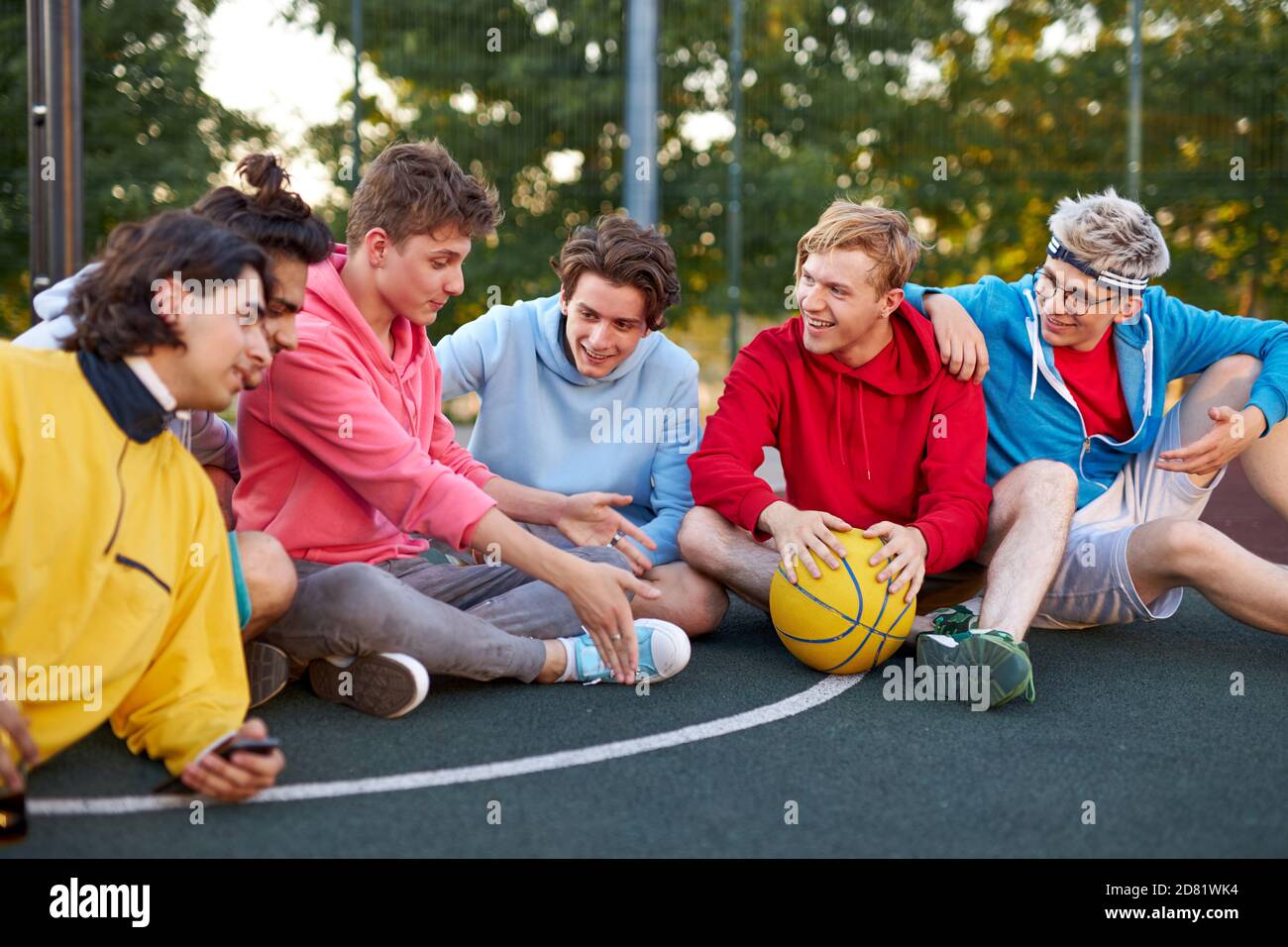 gli adolescenti maschi rilassati riposano dopo i giochi sportivi, la pallacanestro all'aperto in campo. i ragazzi caucasici in abbigliamento casual si divertono a trascorrere il tempo con gli amici Foto Stock