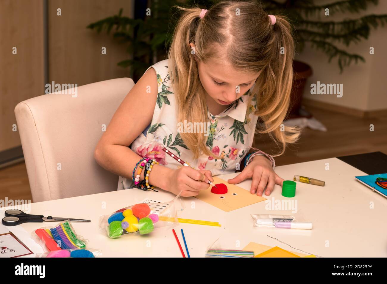 adorabile ragazza con carte colorate, forbici, colla, cannucce, matite, nastri, pizzo sul tavolo makint unico auguri di natale Foto Stock