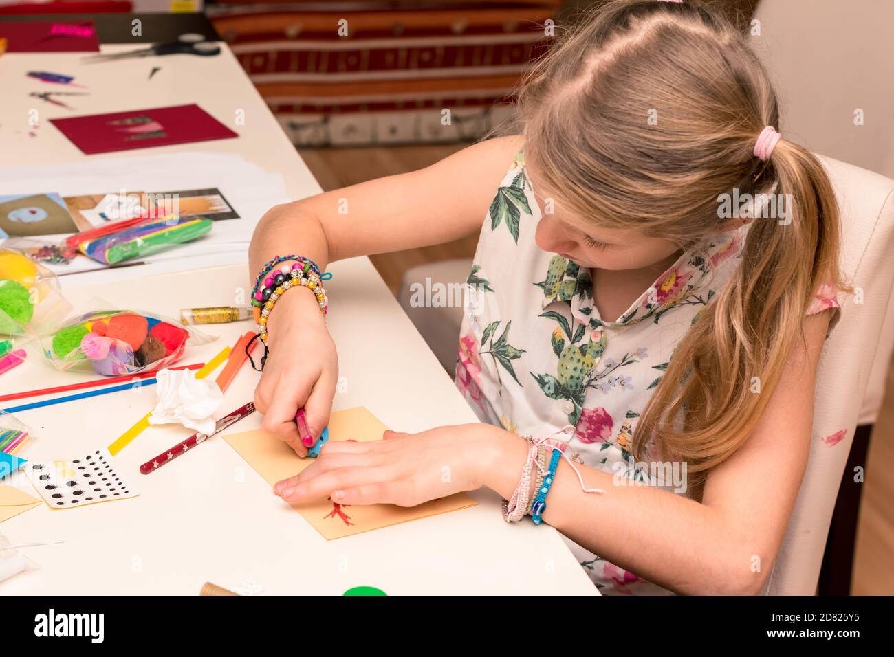 adorabile ragazza con carte colorate, forbici, colla, cannucce, matite, nastri, pizzo sul tavolo makint unico auguri di natale Foto Stock