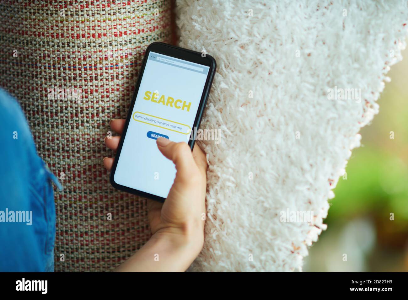 Primo piano su donna con tappeto bianco alla ricerca di servizio di pulizia tappeto su uno smartphone a casa in giornata di sole. Foto Stock