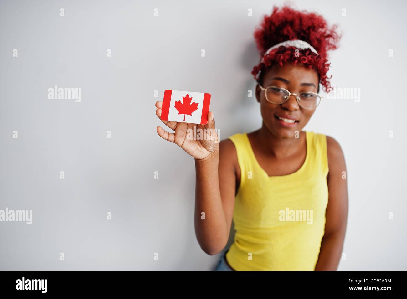 Donna afroamericana con capelli afro, indossare singlet giallo e occhiali, tenere Canada bandiera isolato su sfondo bianco. Foto Stock