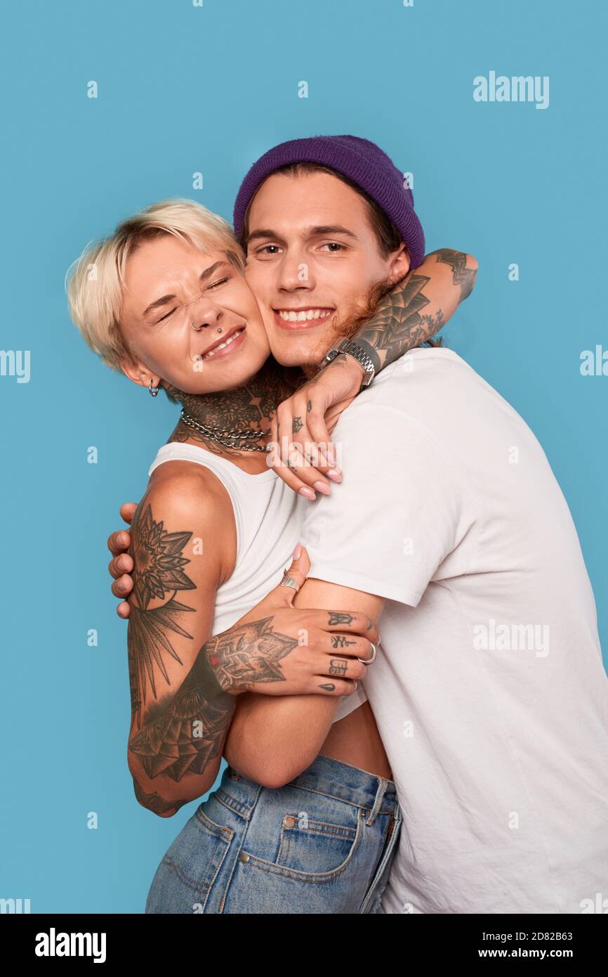 Stile libero. Giovane coppia tatuata in piedi isolato su hugging blu sorridente felice primo piano Foto Stock