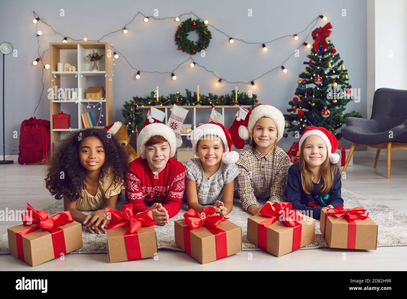 Gruppo di bambini diversi che si trovano sul pavimento vicino a regali di Natale e guardando la macchina fotografica. Foto Stock