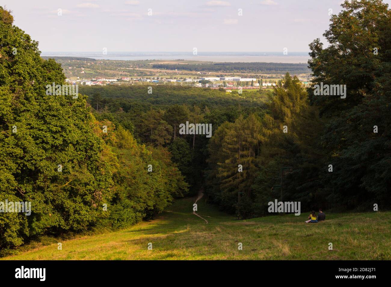 Vista dalla cima della pista di sci al lago fermo con giovane coppia seduta sull'erba, Sopron, Ungheria Foto Stock