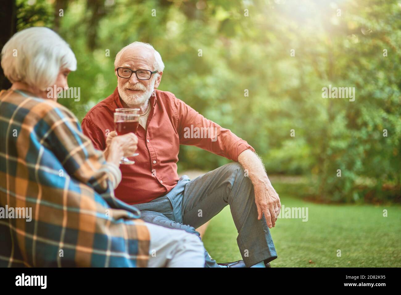 Uomo anziano felice che guarda la moglie mentre tiene i bicchieri con il vino rosso all'aperto. Relazione e concetto di famiglia. Spazio di copia Foto Stock