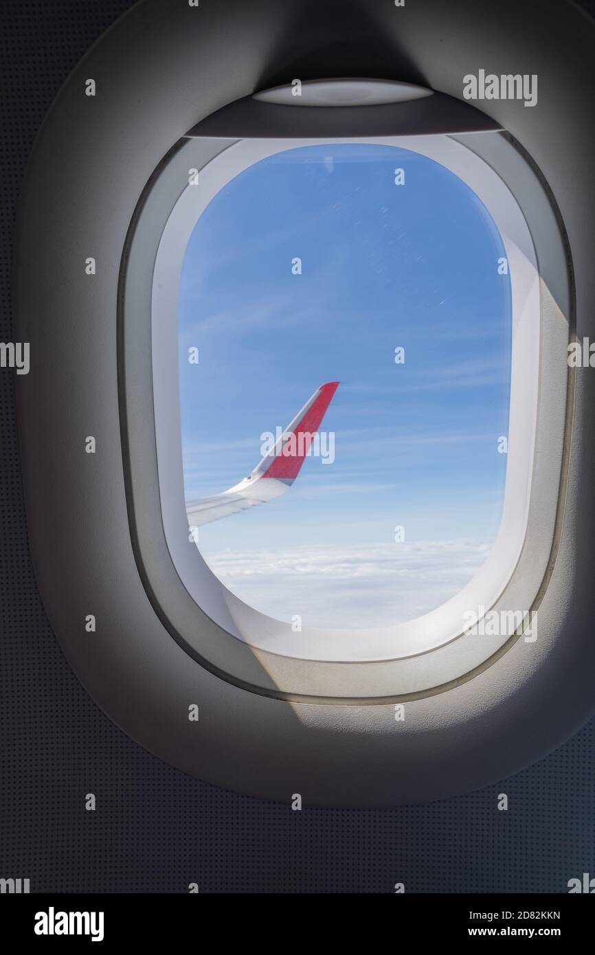 Vista delle ali rosse dell'aereo con il bel cielo blu e le nuvole all'interno della finestra dell'aereo. Foto verticale Foto Stock