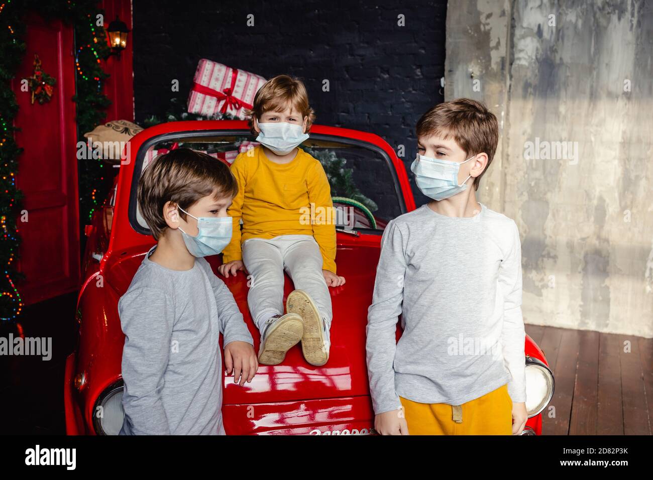 Carino seri fratelli ragazzi in maschere mediche si stanno preparando per il nuovo anno vicino alla vettura di Natale. Vacanza, distanza sociale, soggiorno a casa. Foto Stock