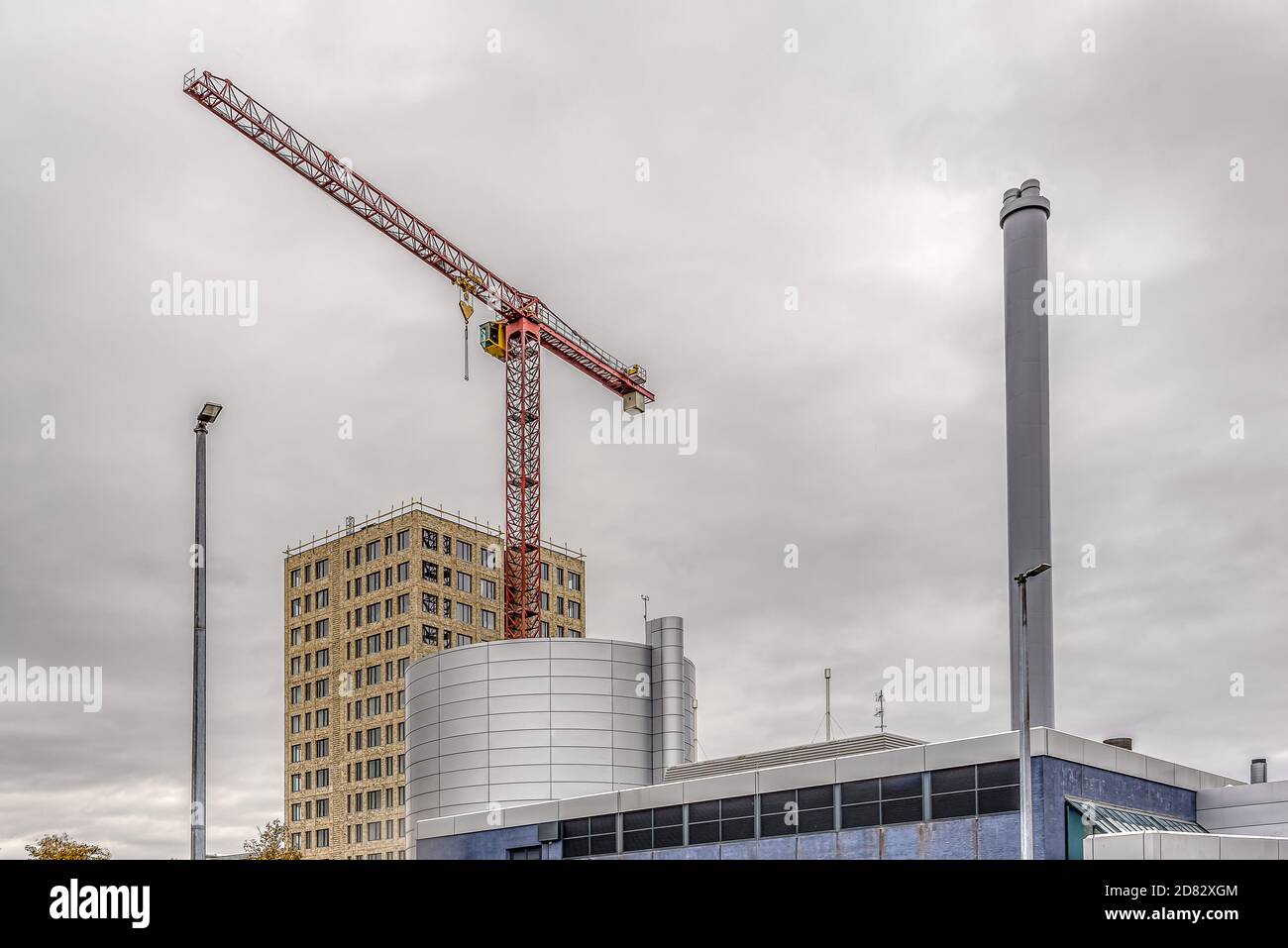 Costruzione di blocchi di appartamenti dietro un camino di impianto di riscaldamento con una gru da costruzione rossa, Frederikssund, Danimarca, 25 ottobre 2020 Foto Stock