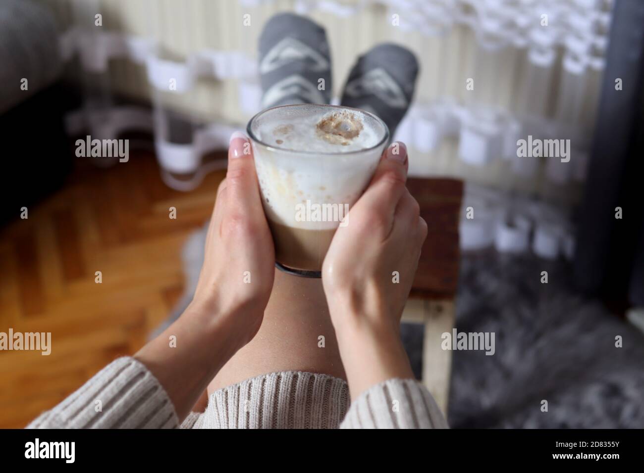 Le mani della ragazza che tengono sulle gambe una tazza di vetro di caffè  con la schiuma grande del latte a casa nel soggiorno. Concetto di bevanda  calda Foto stock - Alamy