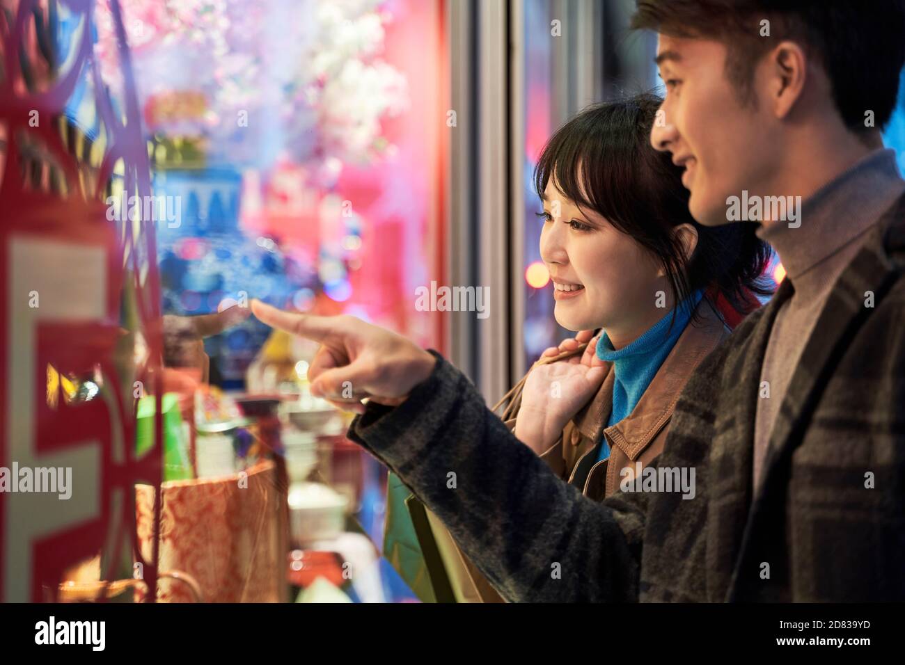 giovane coppia asiatica amorevole che guarda la vetrina e parla felice e sorridente Foto Stock