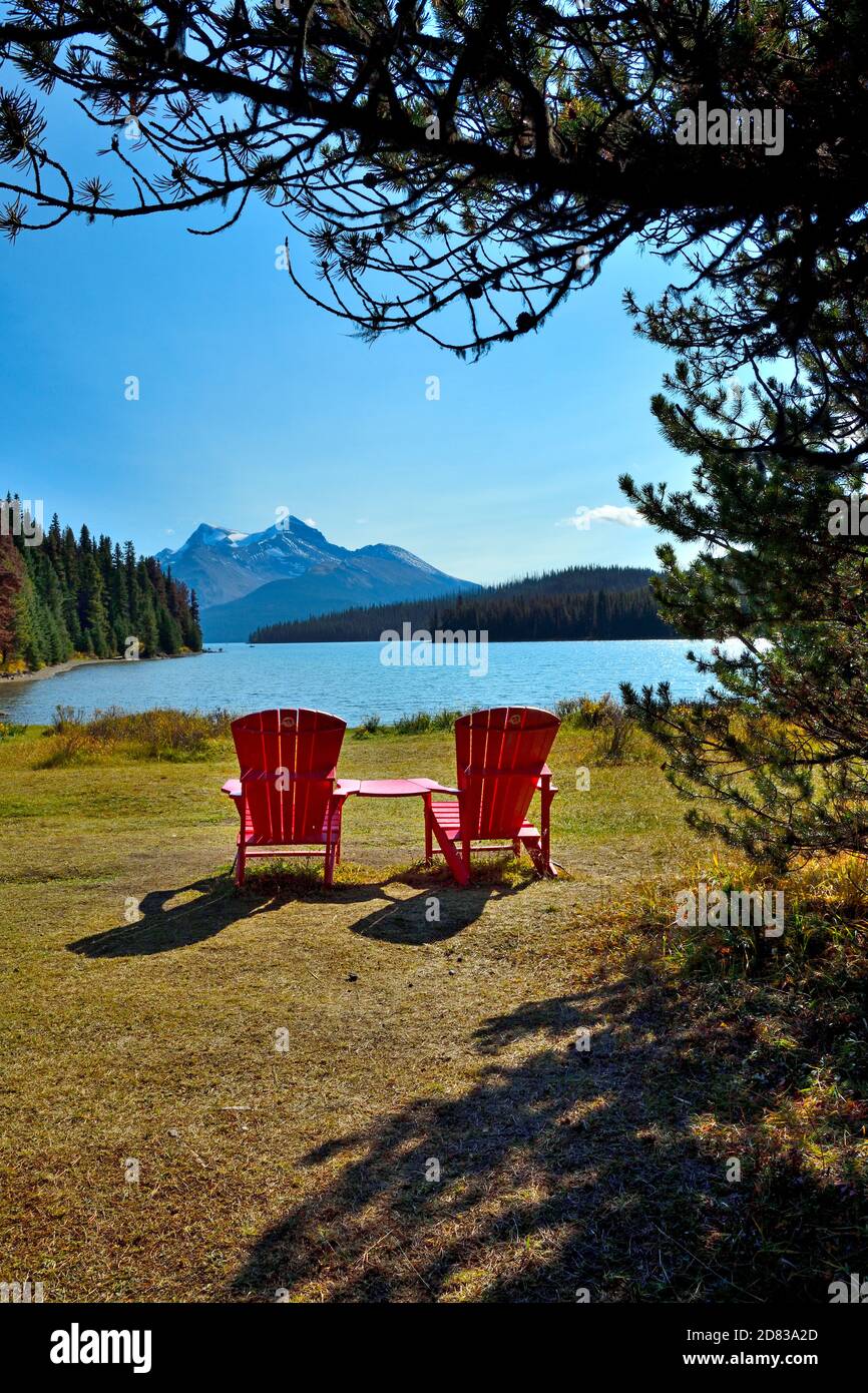Un'immagine verticale di due sedie rosse posizionate per qualcuno per sedersi e godere della vista delle montagne sul lago Maligne nel Jasper National Park in Alberta Canada. Foto Stock