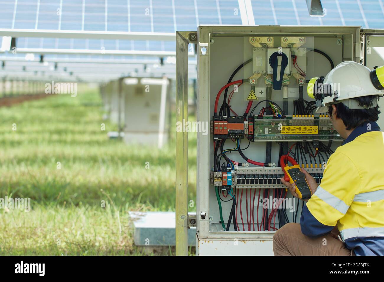 Gli operatori utilizzano il multimetro a pinza per misurare la corrente dei fili elettrici prodotti dall'energia solare per confermare il normale funzionamento dei sistemi. Foto Stock