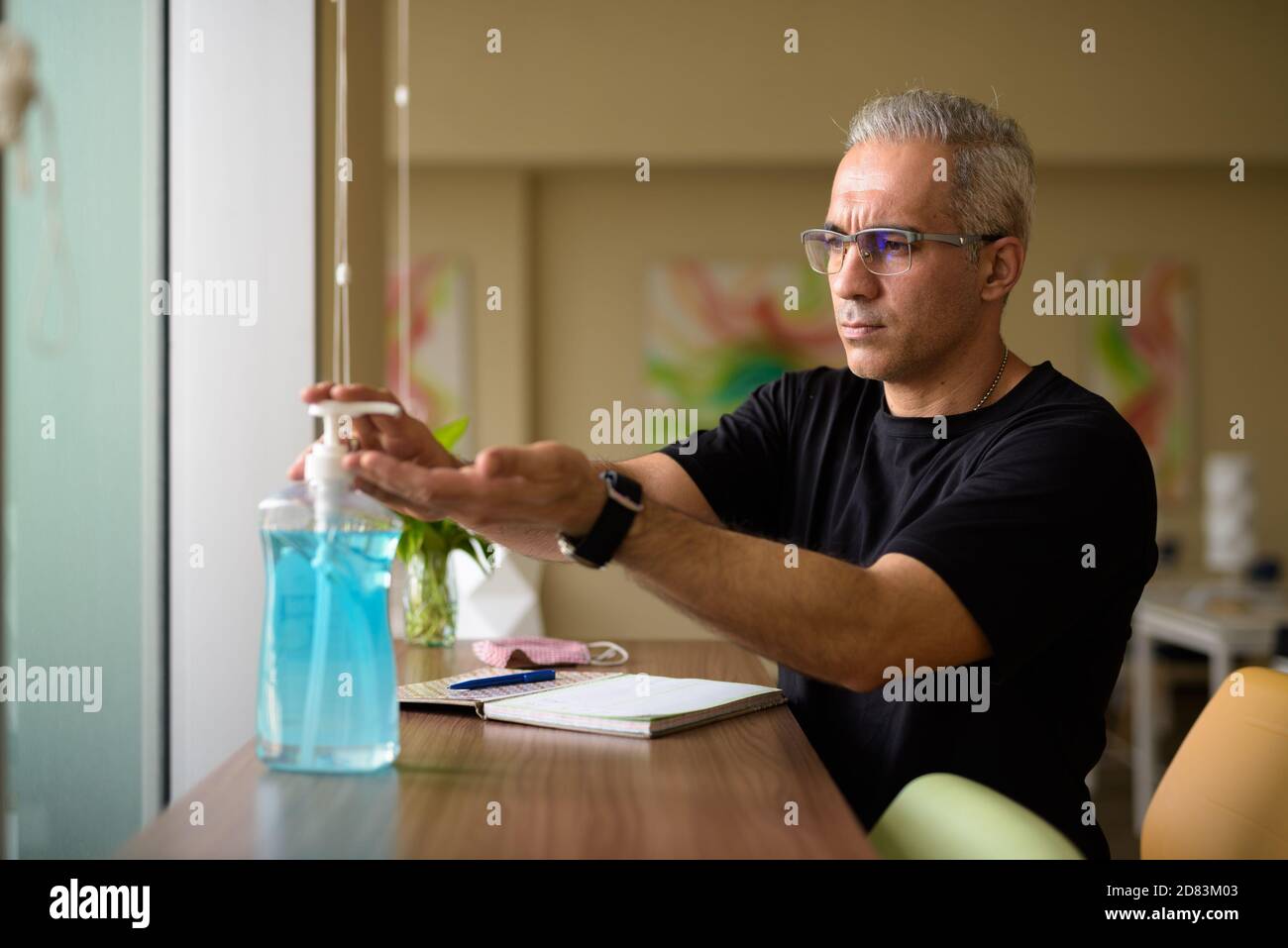 Bell'uomo persiano con i capelli grigi usando l'igienizzatore a mano a. la biblioteca Foto Stock