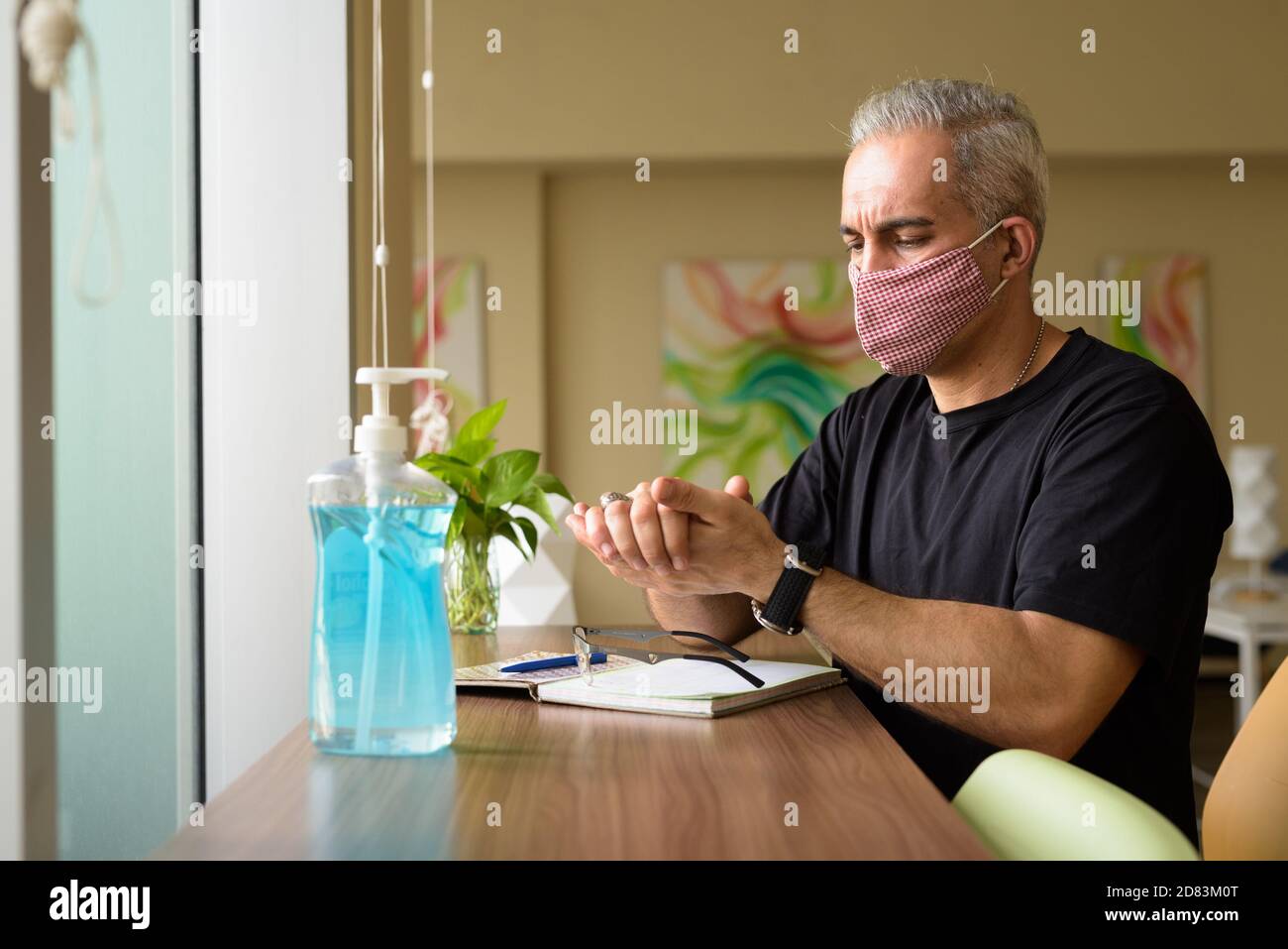 Ritratto di uomo persiano con maschera utilizzando disinfettante a mano a. la biblioteca Foto Stock
