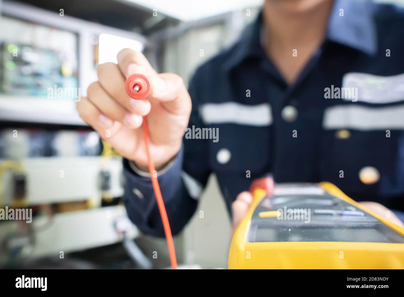 L'estremità positiva del multimetro, tenuta da un ingegnere con un background sfocato, il concetto di utilizzare strumenti digitali per il controllo elettrico ed elettrico Foto Stock