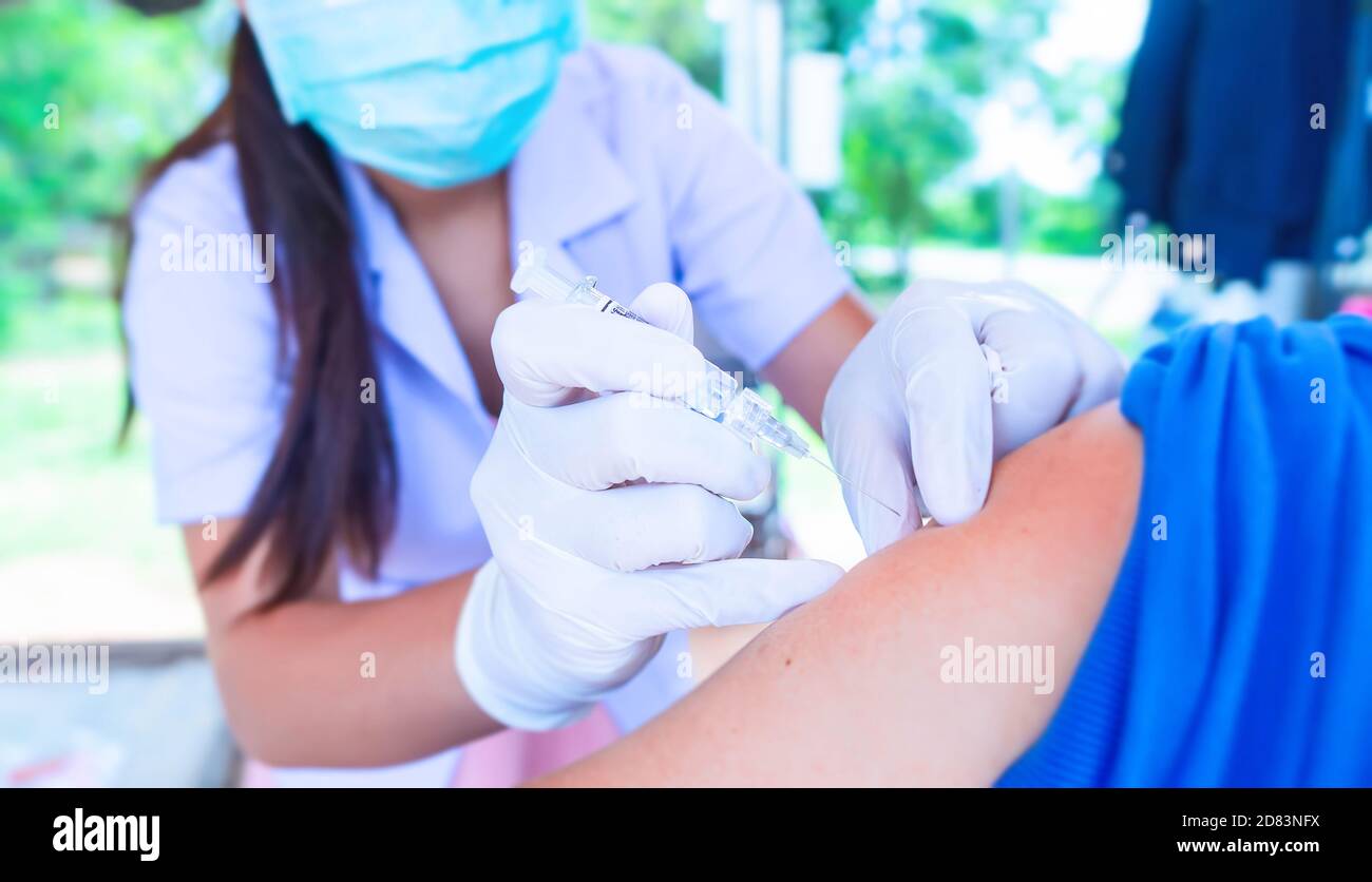 La mano del medico ha tenuto una siringa per vaccinare le persone, e deve indossare una maschera facciale per conformarsi al ministero della sanità pubblica norme in materia di prevenzione Foto Stock