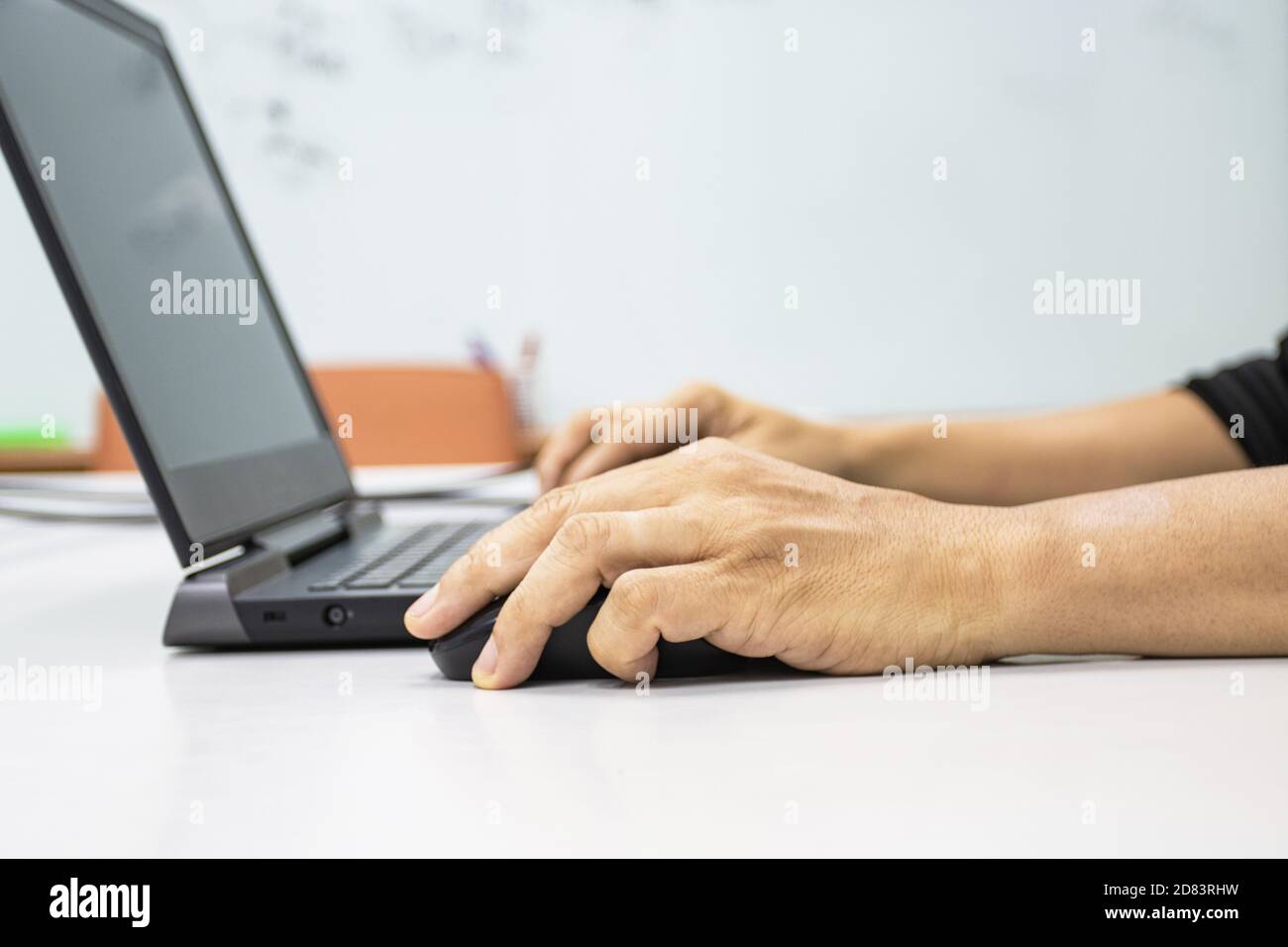 Un uomo seduto con un computer portatile con una mano per tenere un mouse mostra il concetto di sindrome da ufficio con polso weire da tenere premuto il mouse Foto Stock