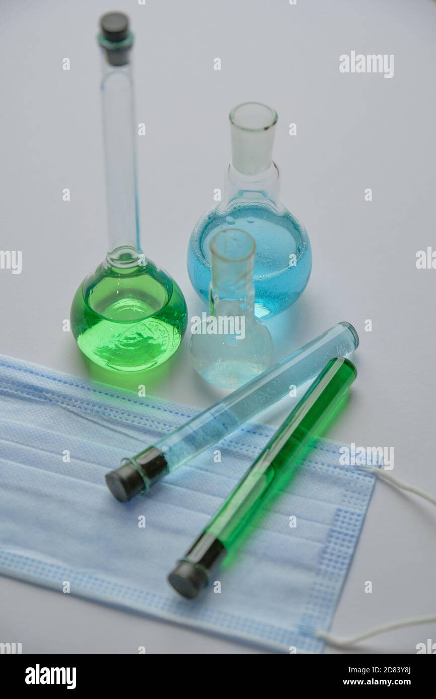 Primo piano immagine verticale della vetreria chimica che si riunisce su una scrivania bianca con maschera facciale. Ricerca Covid Foto Stock
