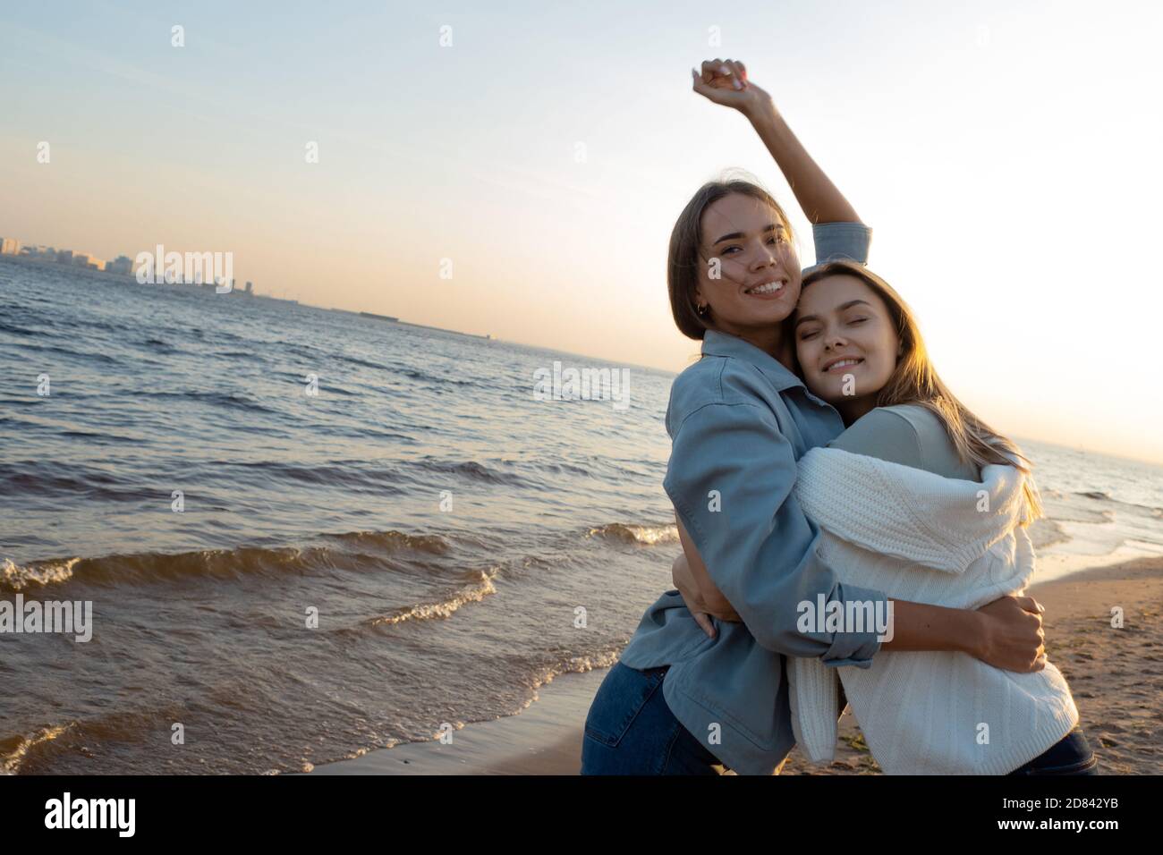 Gli amici si divertono insieme. Giovani donne in spiaggia la sera, abbracciando e ridendo. Foto Stock