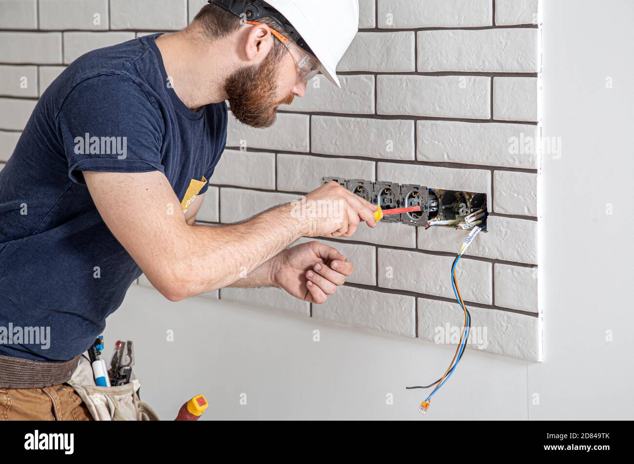 Elettricista costruttore al lavoro, installazione di prese e interruttori.  Professionale in tute con utensile per elettricisti. Sullo sfondo di Foto  stock - Alamy