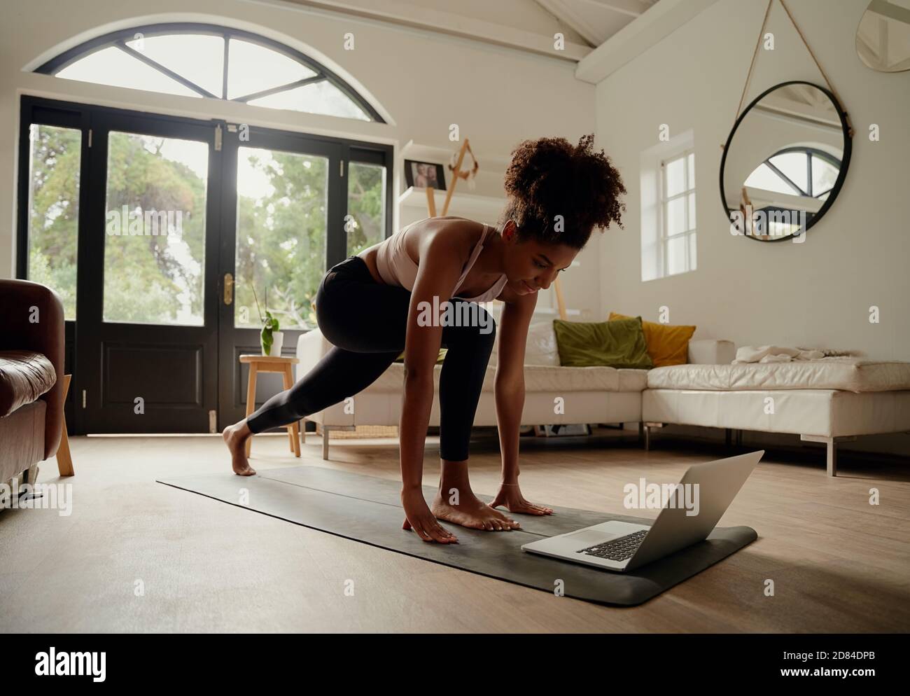 Giovane donna che segue il video sul laptop mentre si esercita sullo yoga tappetino a casa Foto Stock