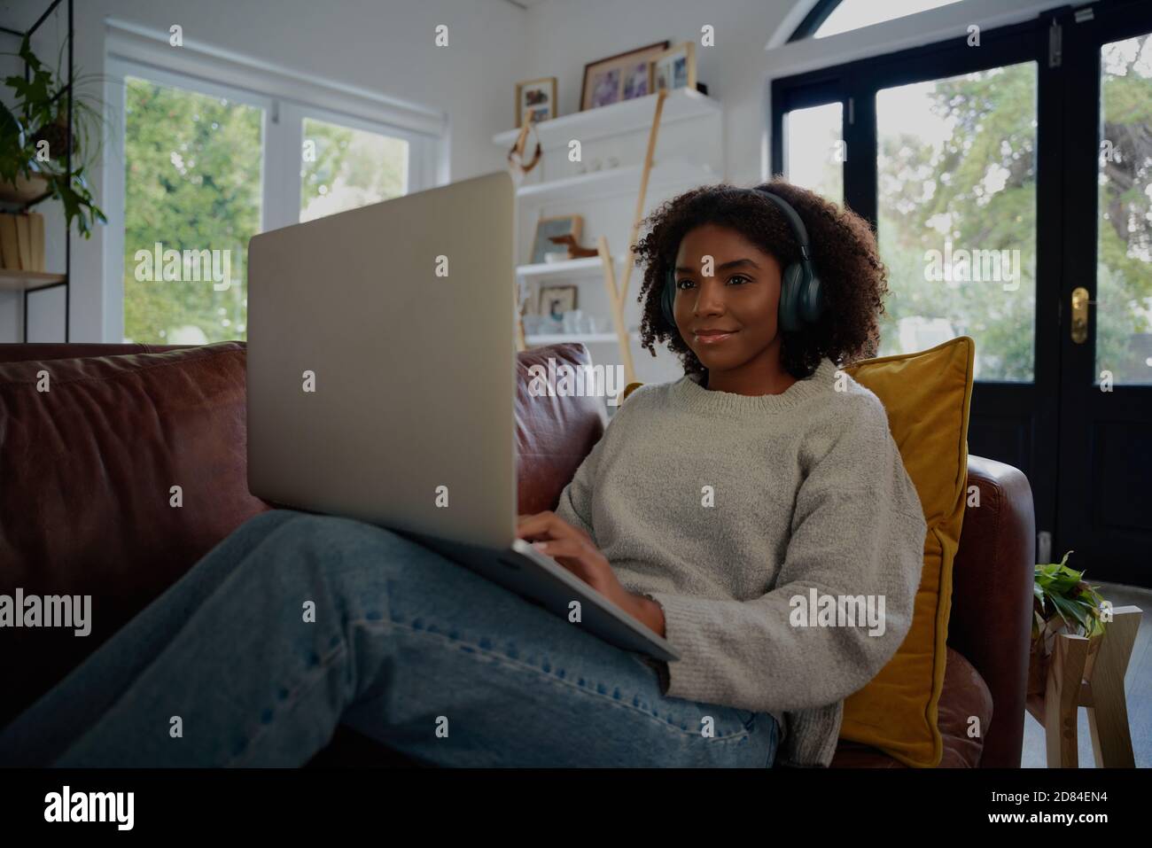 Ritratto di donna africana seduto utilizzando il computer portatile guardando il video con cuffie sul divano Foto Stock