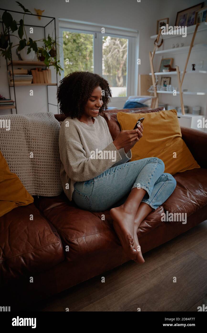 Bella donna africana guardare video su smartphone a casa mentre rilassarsi sul divano Foto Stock