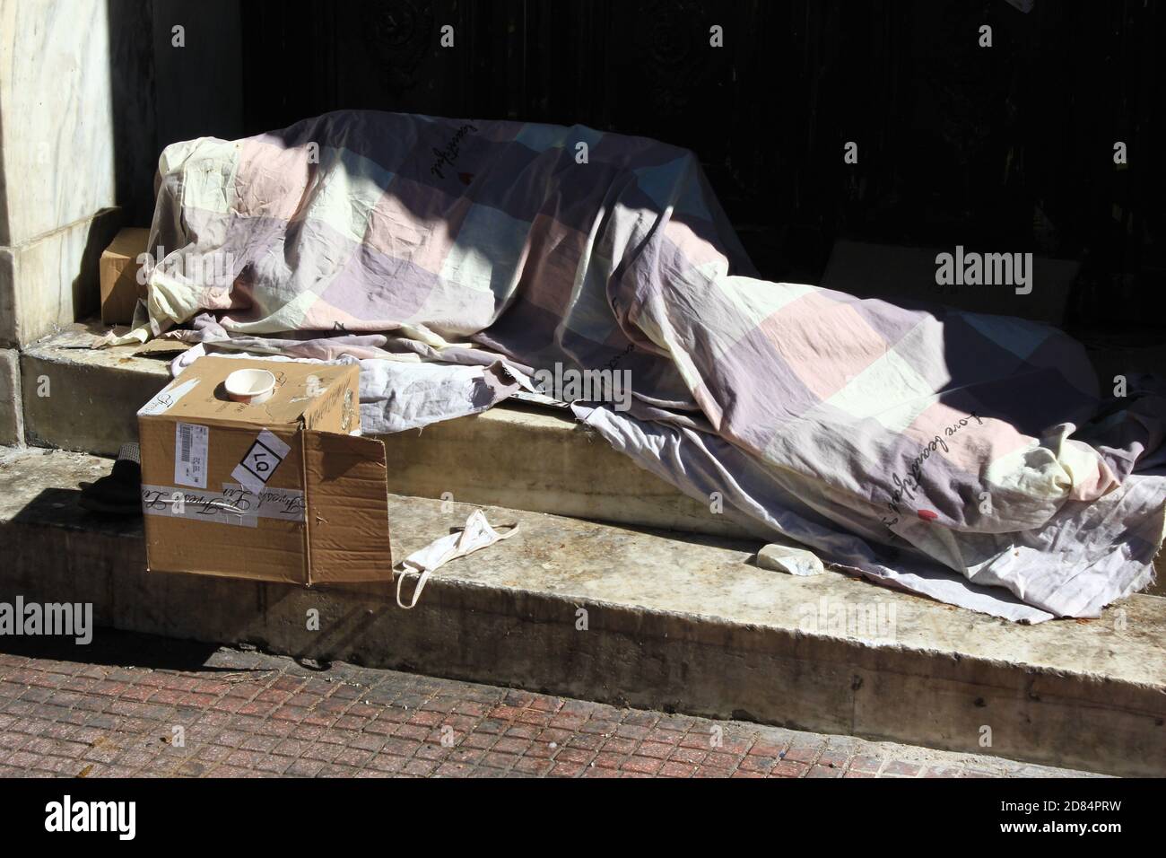 Una persona senza dimora non identificata che dorme di fronte all'ingresso del vecchio edificio nel centro di Atene - Atene, Grecia, 9 ottobre 2020. Foto Stock