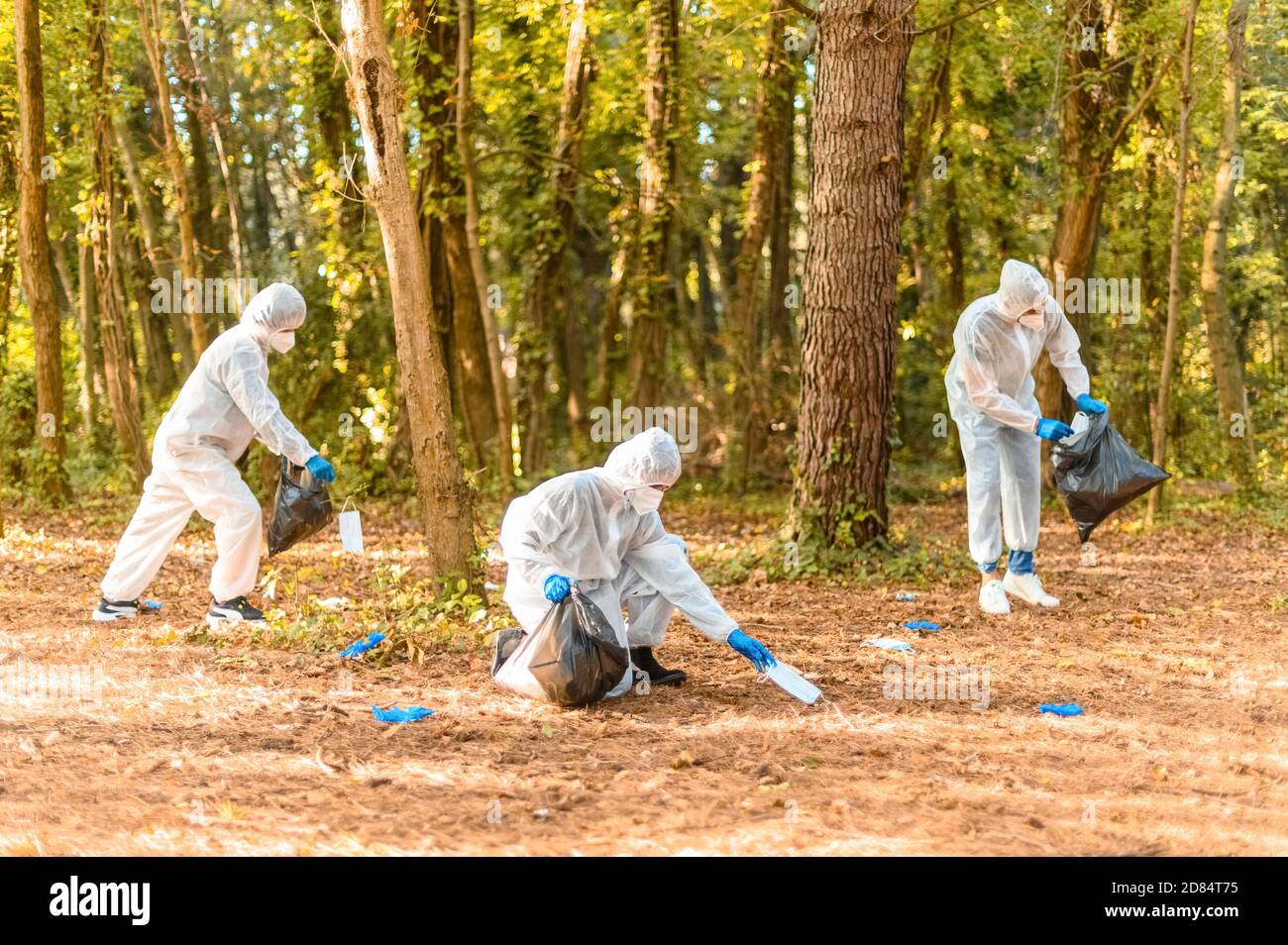 Lavoratori in tuta protettiva con maschere facciali, raccoglie sporche protezioni mediche per covid-19 in un parco - concetto di ecologia e la consapevolezza dopo coronavi Foto Stock