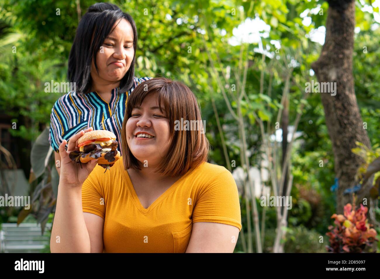 La donna in sovrappeso è in sedia a rotelle. Mangiare un hamburger in cui, ma il suo amico non è felice a causa della preoccupazione per la salute di un amico. Hea Foto Stock