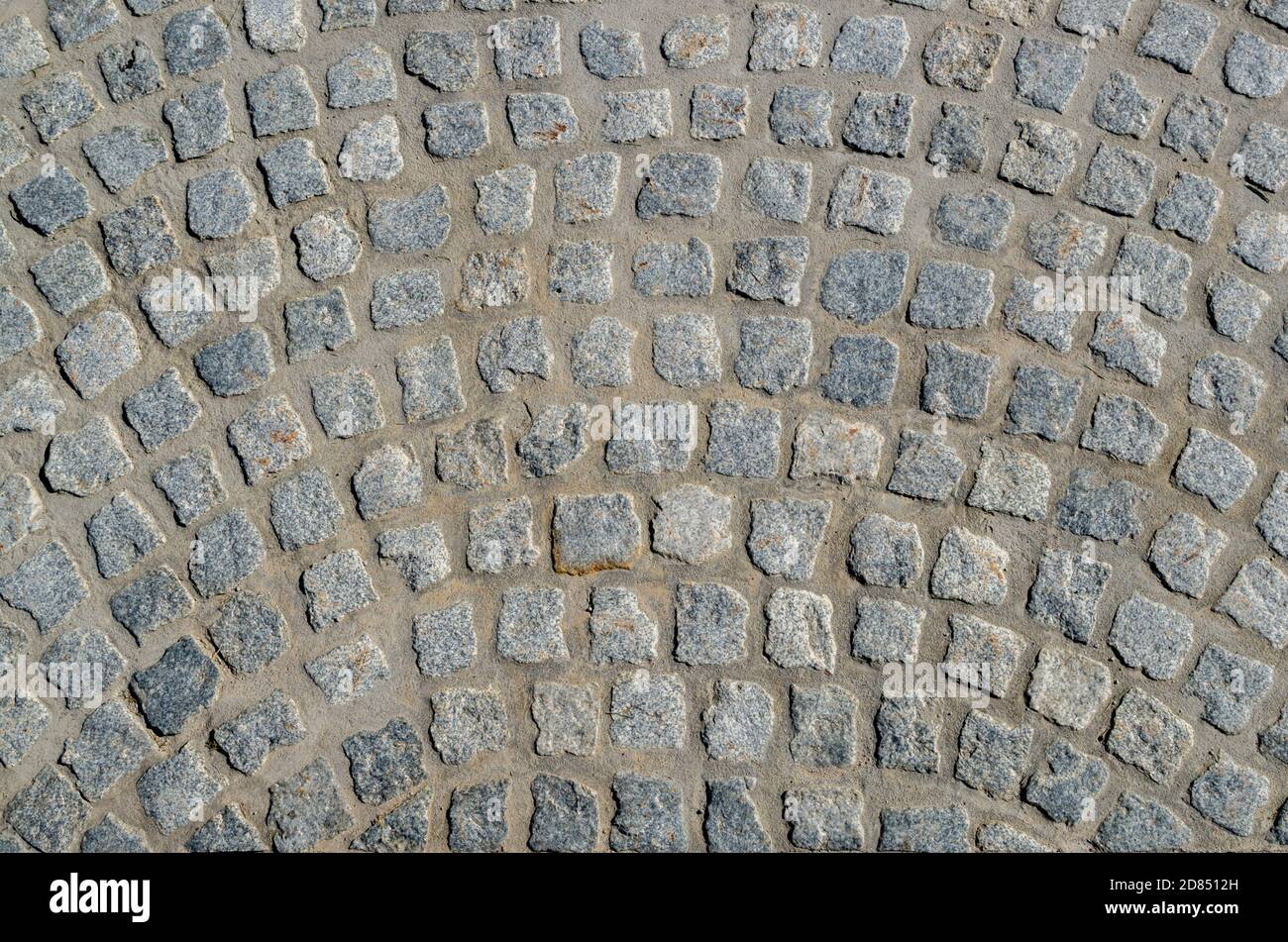 Un frammento di pavimentazione lastricata con blocchi di pietra grigiosa quadrata con bordi irregolari sotto forma di strisce arcuate semicircolari. Foto Stock