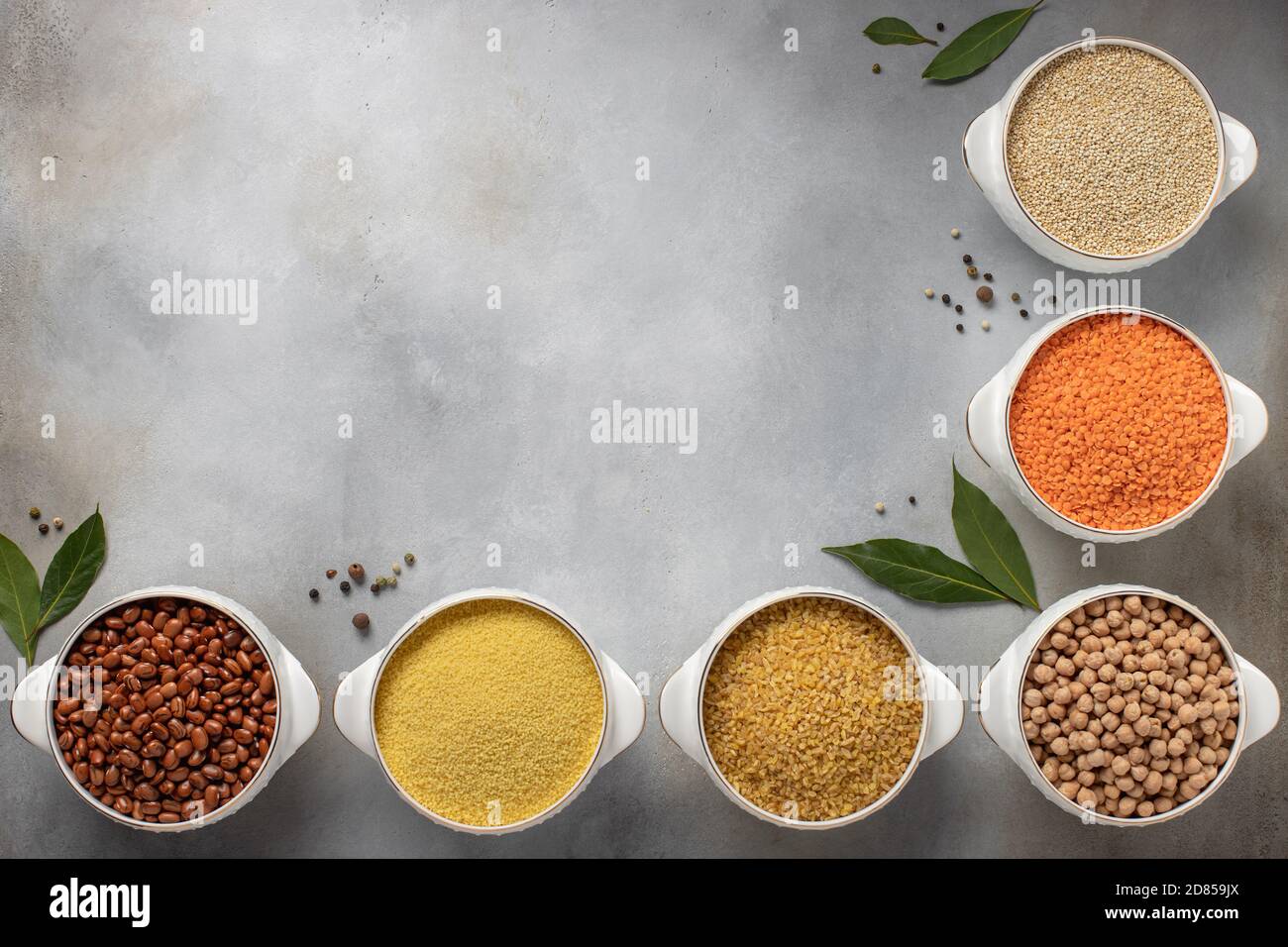 vari tipi di cereali assortiti (quinoa, lenticchie, ceci, bulgur, couscous, fagioli) e spezie. struttura per cibo, posto per testo. sfondo grigio, vista dall'alto Foto Stock