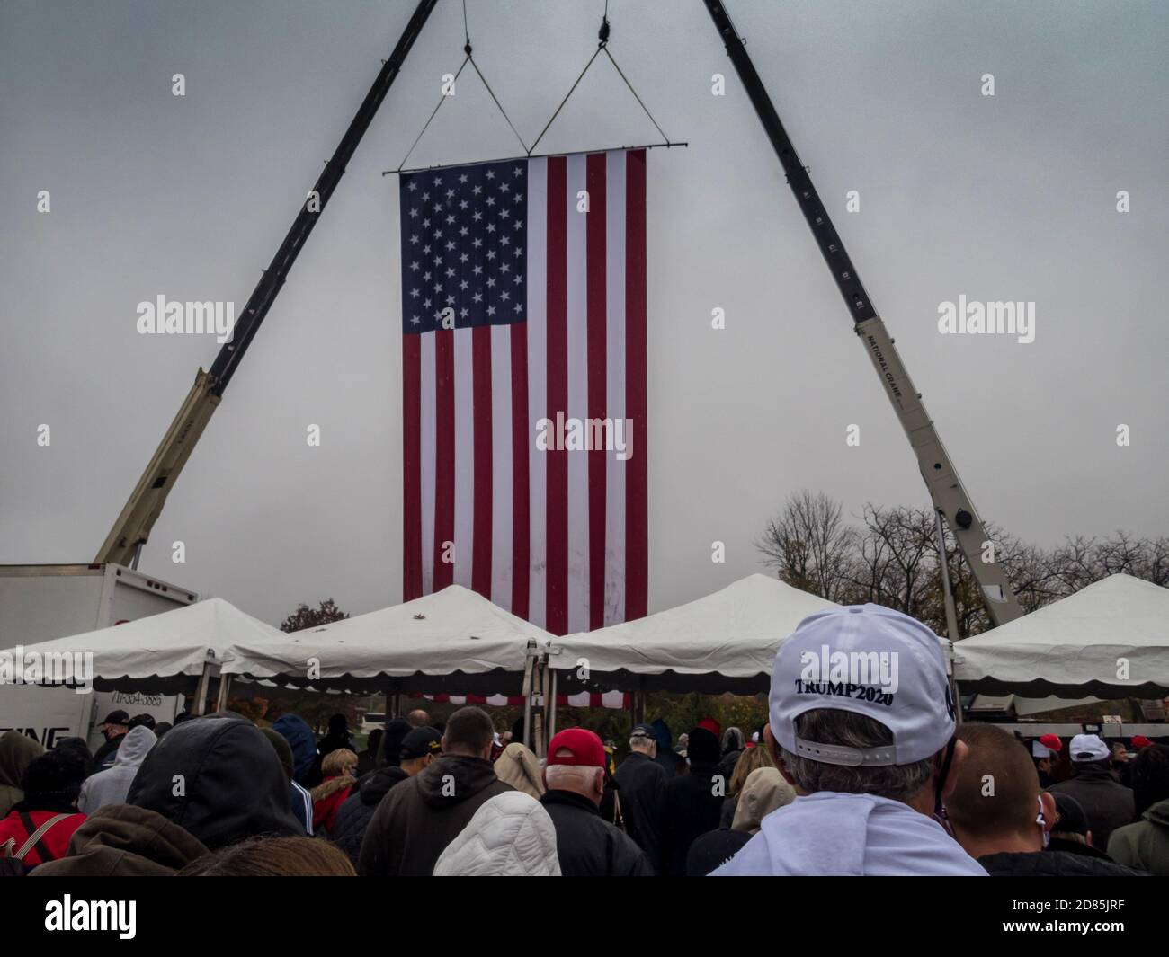 Allentown, PA / USA - 26 ottobre 2020: La bandiera americana enorme pende dalle gru mentre la gente entra nel rally di Trump in una giornata fredda e piovosa Foto Stock