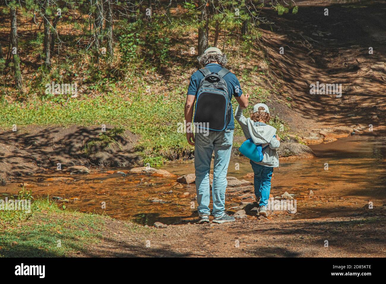 Padre e figlio attraversano il torrente nella foresta. Uomo e bambino con zaini sullo sfondo della foresta. Concetto di viaggio con i bambini. Stile di vita. Foto Stock