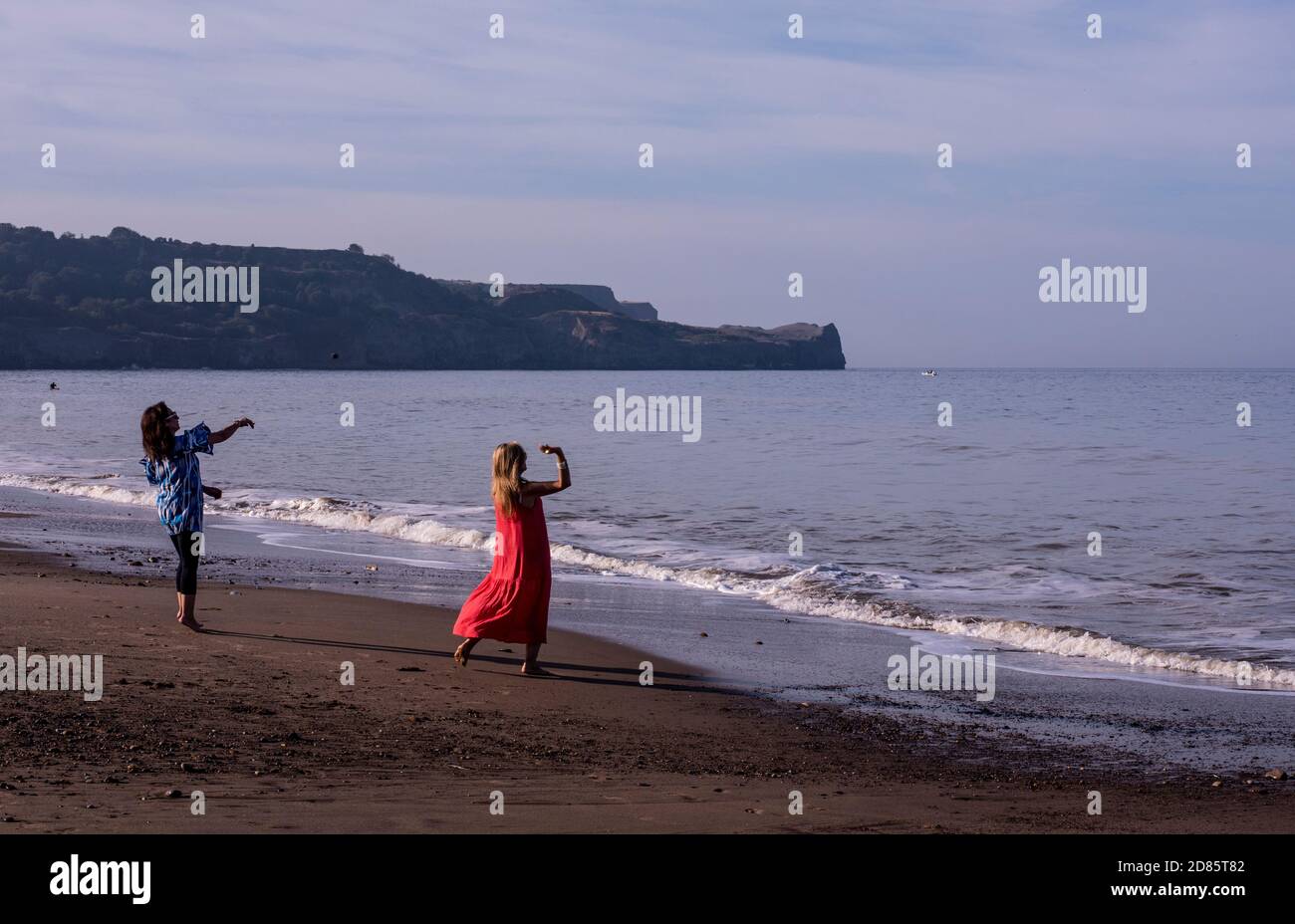 Due donne che gettano ciottoli in mare sulla spiaggia, Whitby, Inghilterra, Regno Unito Foto Stock