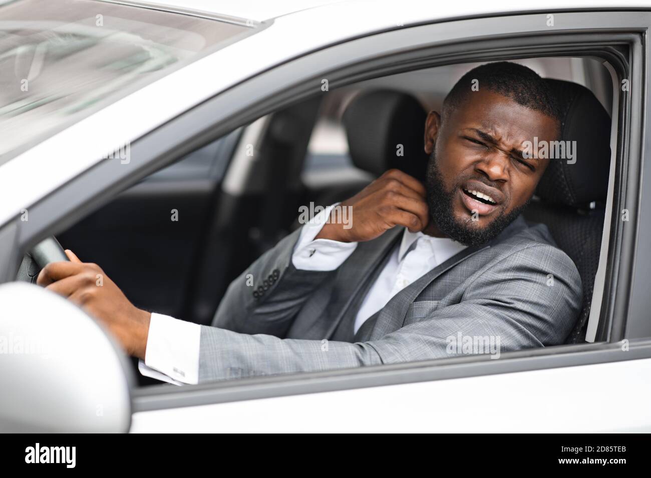 Uomo d'affari africano stressante che stacca la camicia mentre guida l'automobile Foto Stock