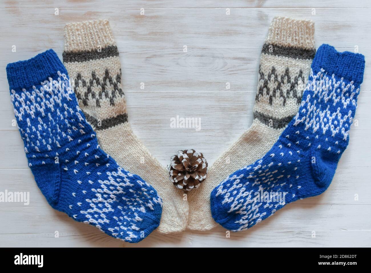 Calze di lana blu e beige per l'inverno e cono di pino su superficie di  legno bianco. Calze calde in lana per stagione fredda e coni di pino su  dorso di legno