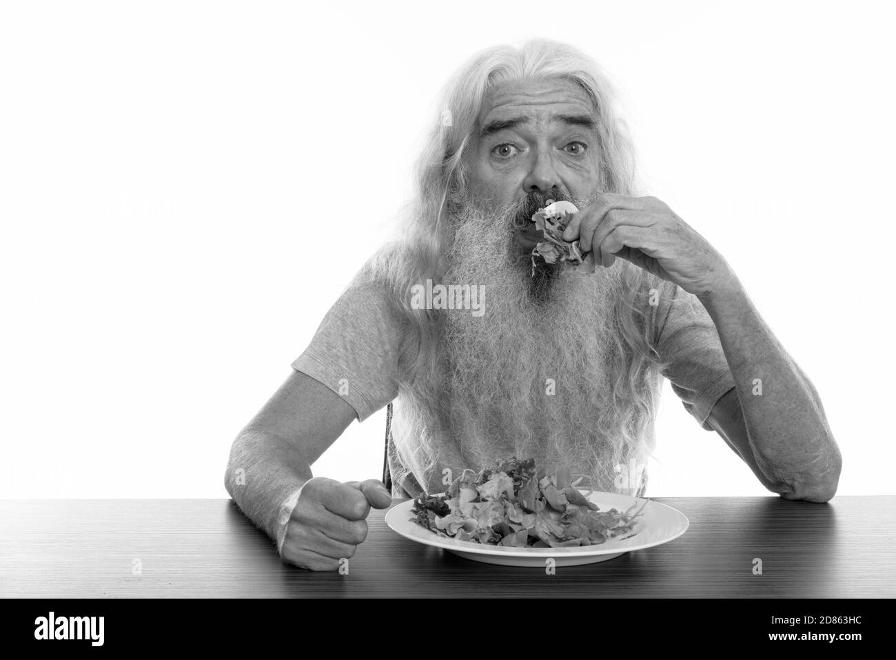 Studio shot di senior uomo barbuto mangiare piatto di insalata sul tavolo di legno Foto Stock