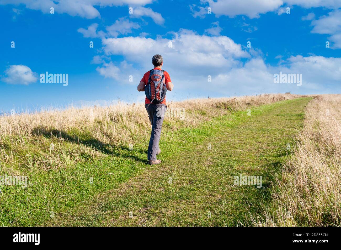 Vista posteriore di un uomo maturo che cammina sul sentiero costiero di Cleveland Way sotto un cielo blu. North Yorkshire, Inghilterra. REGNO UNITO Foto Stock