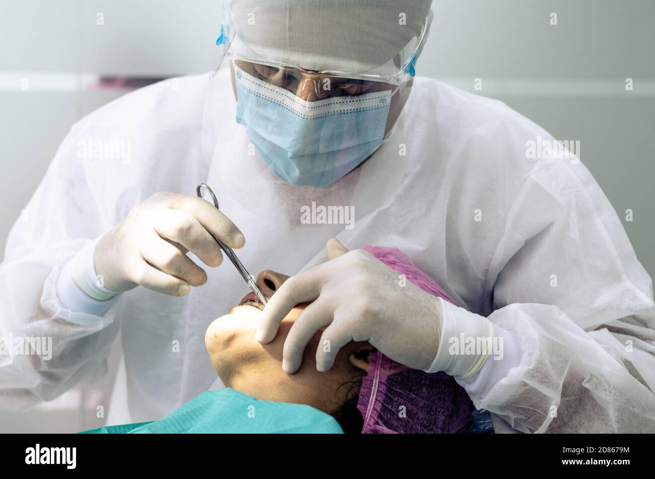 Il dentista o medico indossa un abito medico bianco, una maschera e occhiali protettivi sullo sfondo dell'ufficio del dentista. Concetto di salute e protezione Foto Stock