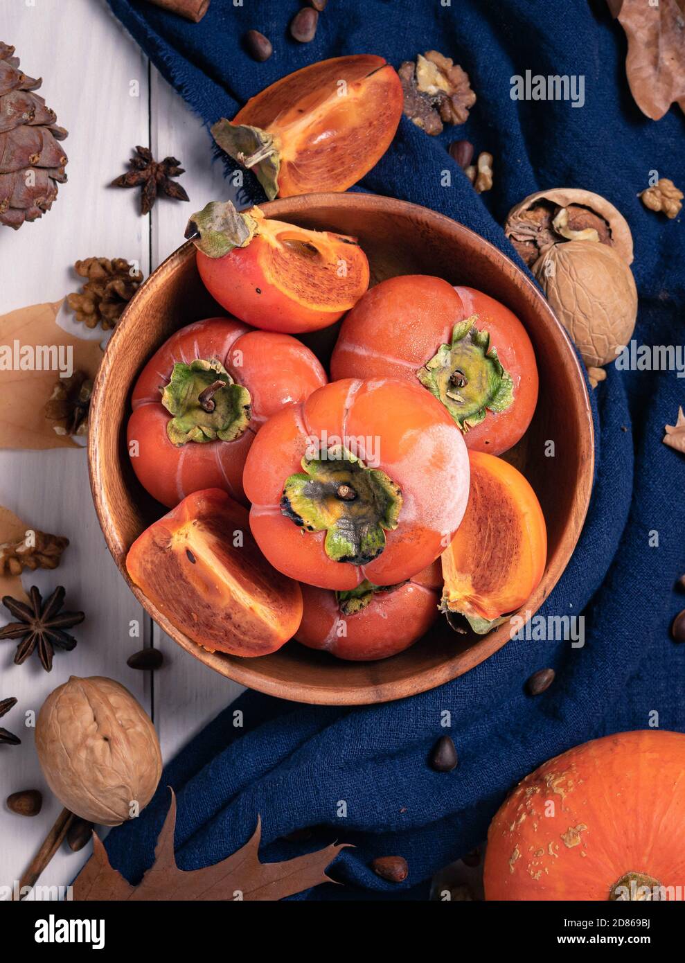 regali di autunno, vista dall'alto, persimmons maturi in una ciotola di legno su uno sfondo con noci, foglie e un cono di pino Foto Stock