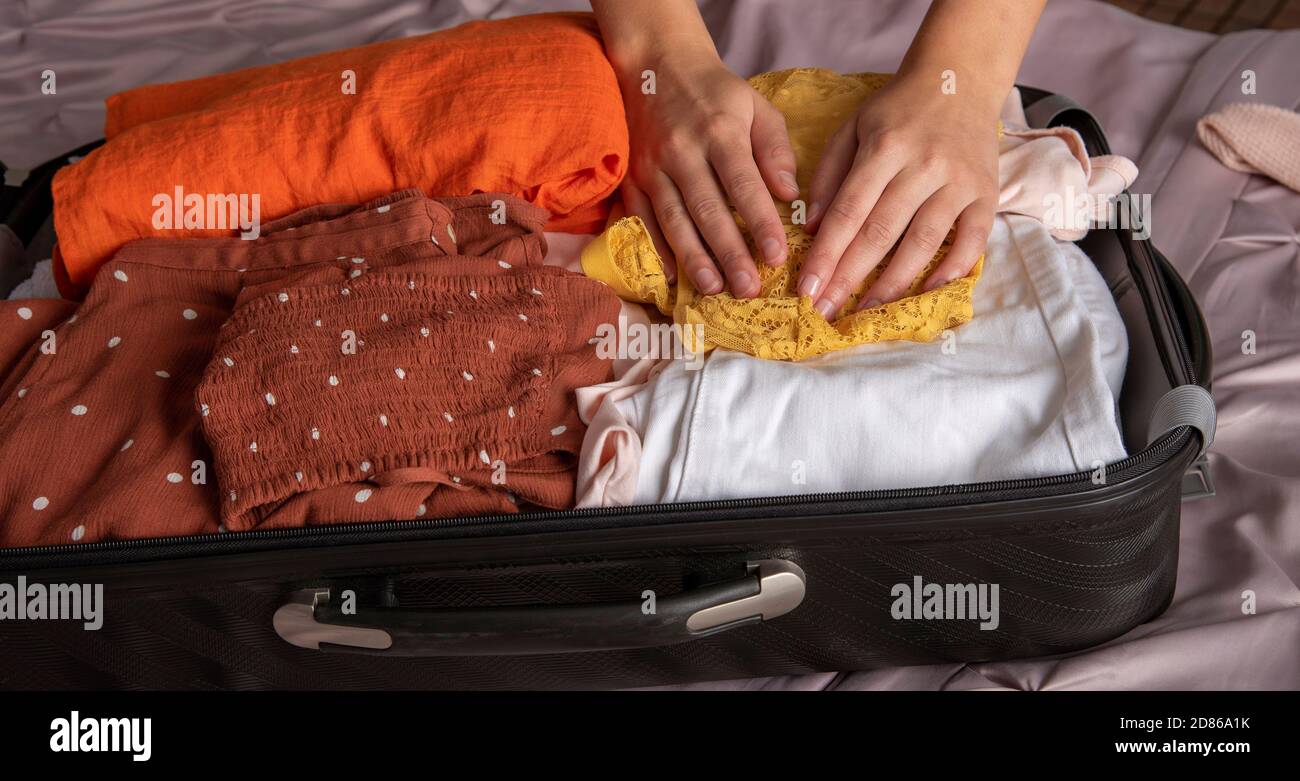 Inghilterra, Regno Unito, 2020. Le mani della donna finiscono con gli abiti da imballaggio nella valigia per le vacanze. Foto Stock