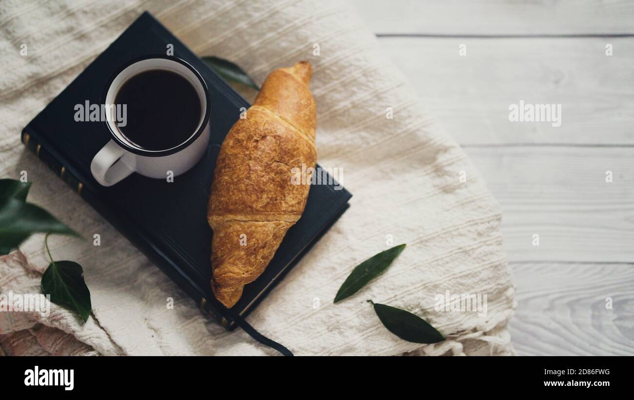 Piatto di croissant appena sfornati con un caldo fresco tazza di caffè su un libro di lettura rilassante mattina di umore accogliente atmosfera di colazione semplice Foto Stock