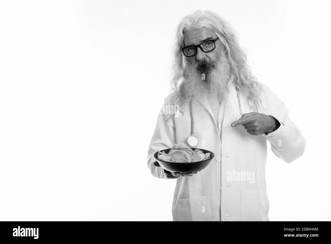 Studio shot di senior uomo barbuto medico azienda e puntando alla ciotola di patatine Foto Stock