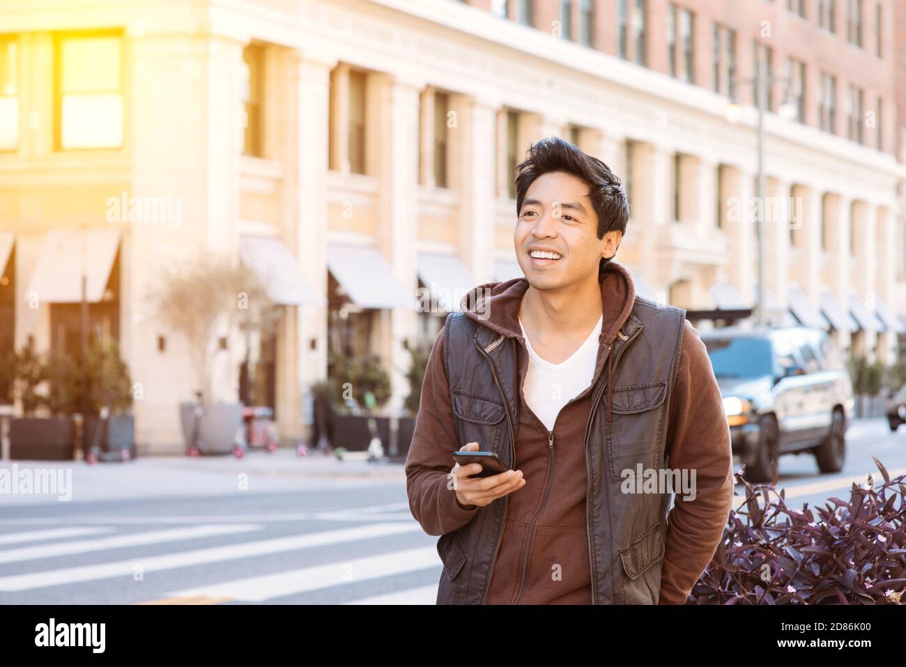 Il maschio asiatico sorride ed è felice di aspettare la sua cavalcata Condividi mentre tieni lo smartphone - trasporto basato su app - Città - giorno Foto Stock
