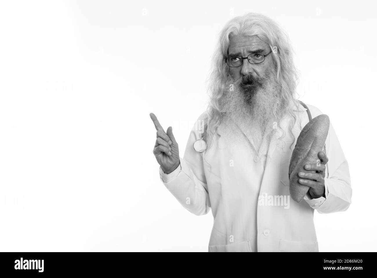 Studio shot di senior uomo barbuto pensiero medico mentre si tiene il pane e puntare il dito fino Foto Stock